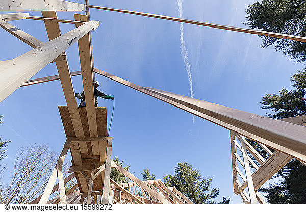 Niedriger Blickwinkel eines Zimmermanns  der einen Schlauch ausbreitet  um die Dachspitze zu erreichen