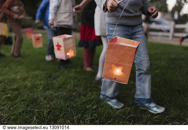 Niedriger Teil von Kindern  die beim Gehen auf dem Feld beleuchtete Papierlaternen tragen