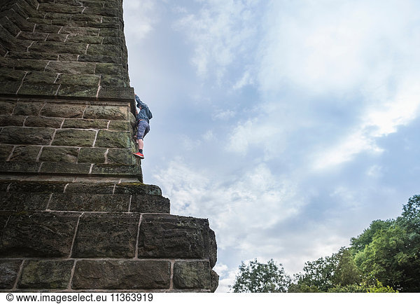 Niedrigwinkelansicht eines Jungen  der an einer Steinwand klettert