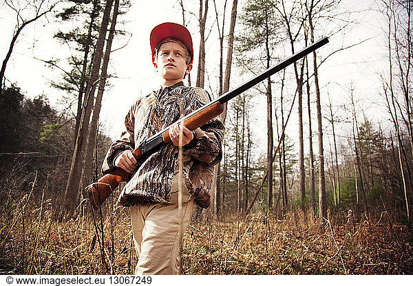 Niedrigwinkelansicht eines Jungen  der beim Waldspaziergang ein Gewehr hält