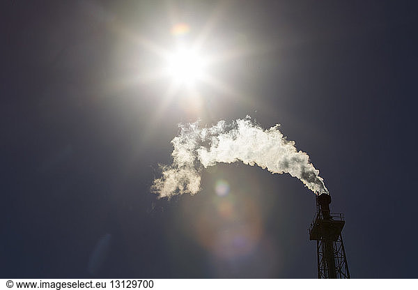 Niedrigwinkelansicht von Rauch aus dem Schornstein einer Ölraffinerie an einem sonnigen Tag