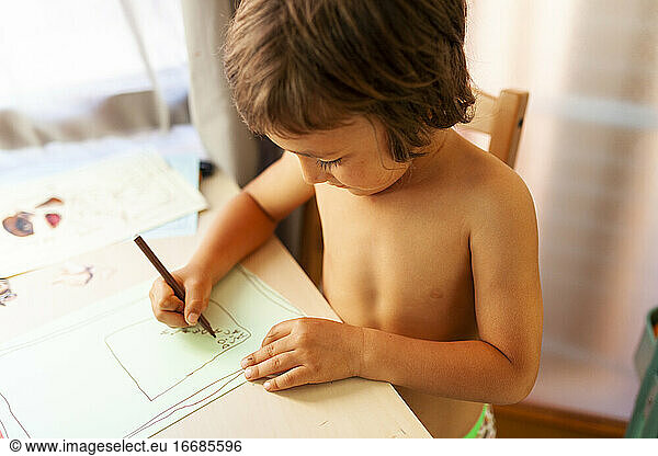 no shirt little boy sitting on table drawing at home