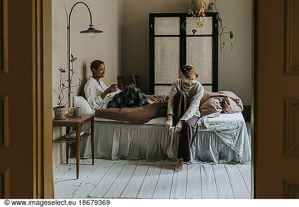 Non-binary couple talking together while sitting on bed at home