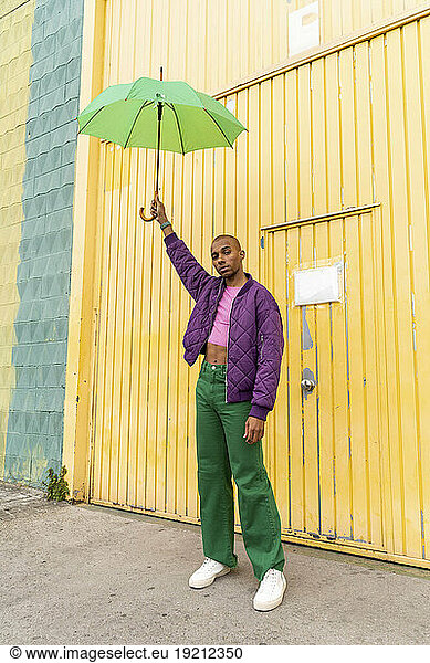Non-binary person holding umbrella in front of yellow shutter door
