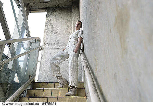 Non-binary person leaning on wall at staircase
