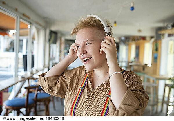 Non-binary person wearing headphones listening to music in cafe