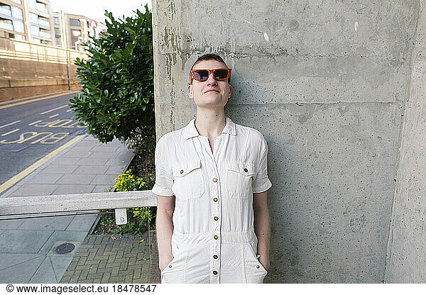 Non-binary person wearing sunglasses leaning on wall