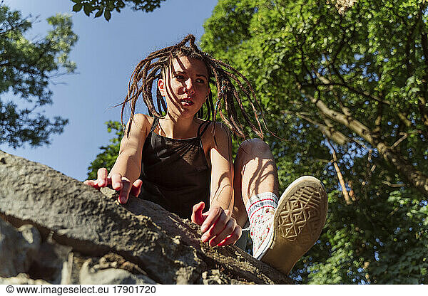 Non-binary person with locs climbing on stone wall