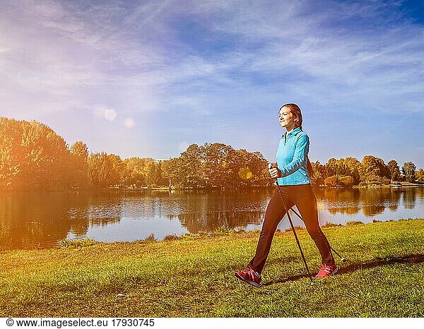 Nordic-Walking-Abenteuer und Trainingskonzept  Frau wandert mit Nordic-Walking-Stöcken im Park. Mit Lichtleck und Linsenreflexion