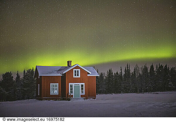 Nordlichter über verschneitem Holzhaus