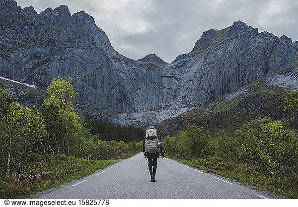 Norway  Lofoten Islands  Backpacker walking down road in mountain landscape