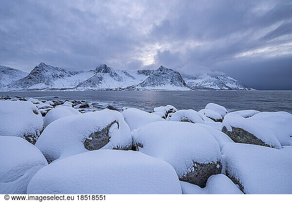 Norway  Troms og Finnmark  Snow covered boulders at Tungenest Rasteplass with fjord and snowcapped mountains in background