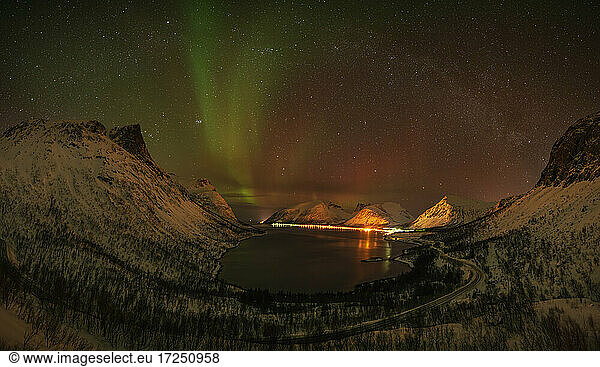 Norwegen  Tromso  Bergsbotn  Blick auf die Aurora Borealis über dem beleuchteten Fjorddorf auf der Insel Senja