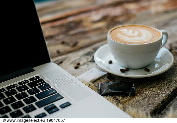 Notebook laptop and creative coffee cup with sugar on old table.