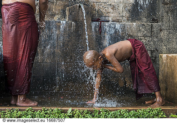 Novice shirtless monks bathing under running water outdoors  near Hsipaw  Myanmar