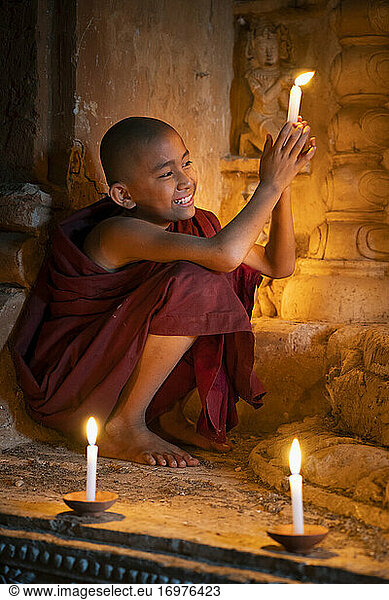 Novizenmönch hält brennende Kerze und lächelt in einem mit Kerzen beleuchteten Tempel  UNESCO  Bagan  Region Mandalay  Myanmar