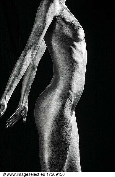 Nude Caucasian woman with silver body paint standing  side view