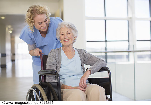 Nurse and aging patient smiling in hospital corridor