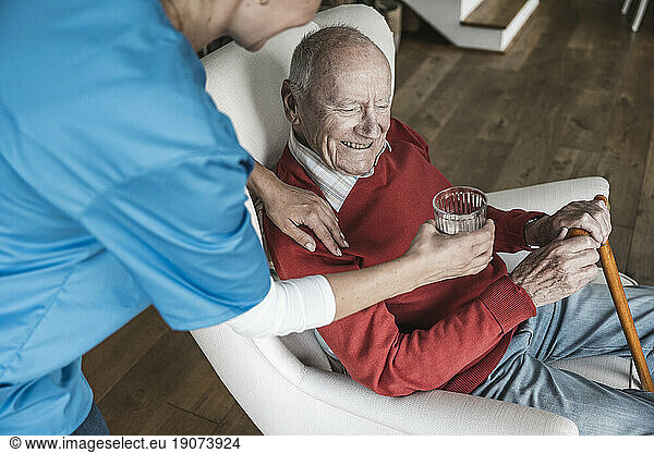 Nurse giving water to senior man at home