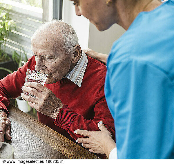 Nurse taking care of senior man drinking water at table