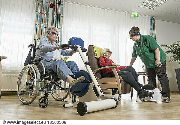 Nurse with senior women exercising on exercise bike in rest home