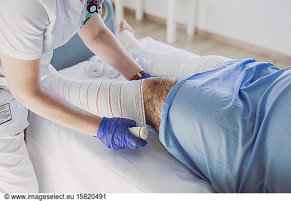 Nurse wrapping bandage around patient's leg in hospital bed