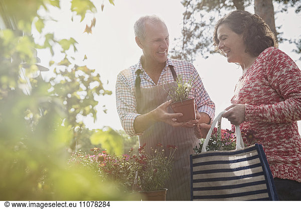 Nursery plant worker showing potted flowers to woman