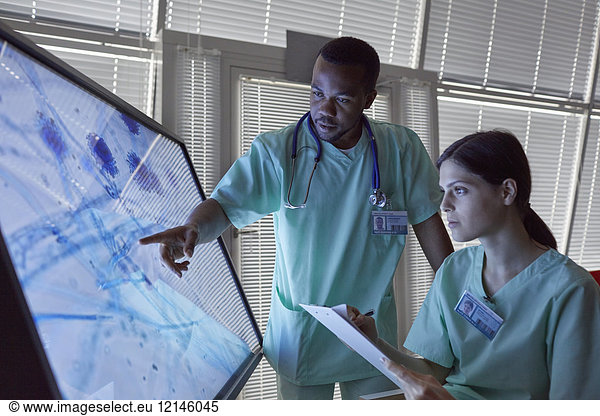 Nurses with clipboard examining magnified microscope slide on computer monitor
