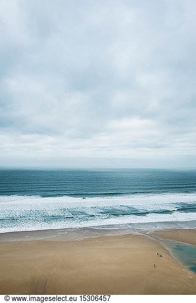 Ocean waves crashing onto a sandy beach under a cloudy sky.