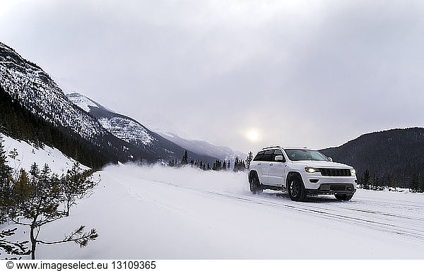 Off-road vehicle moving on snowy field against cloudy sky