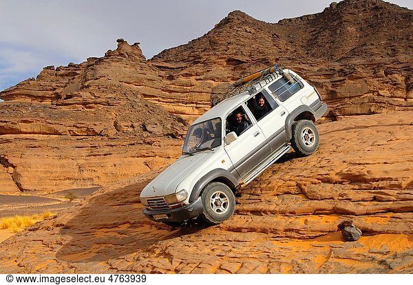 Off-road vehicle with tourists on board traversing a steep rock passage  Acacus Mountains  Sahara desert  Libya