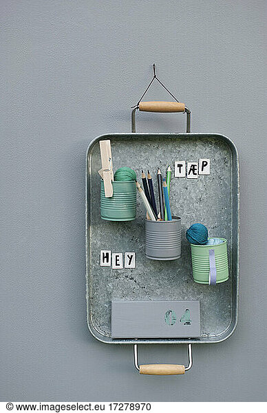 Office supplies in cans attached to metal tray hanging on wall