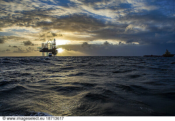 Offshore drilling platform during sunrise with work vessel