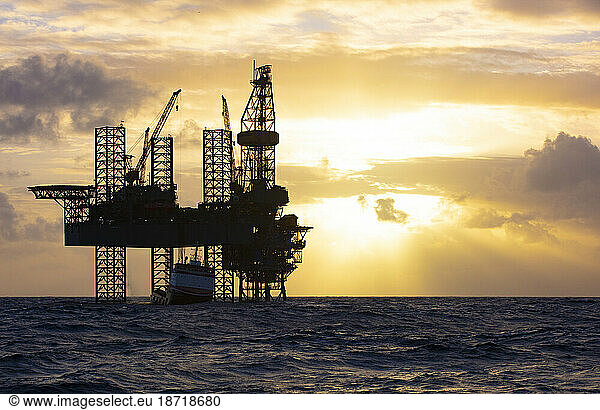 Offshore drilling platform during sunrise with work vessel