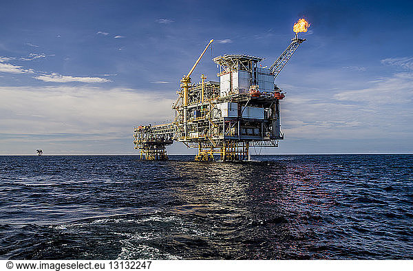 Offshore platform in sea against cloudy sky