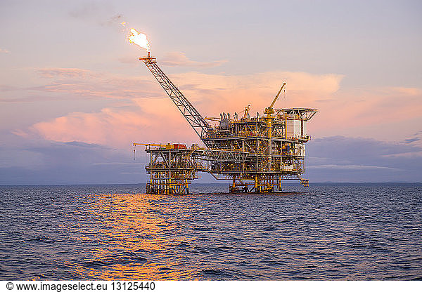 Offshore platform in sea against sky during sunset