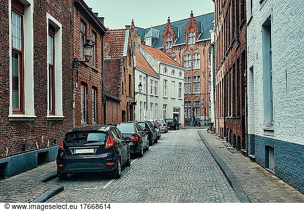 Old town Brugge street with cobblestone road with parked cars and old medieval houses  Bruges  Belgium