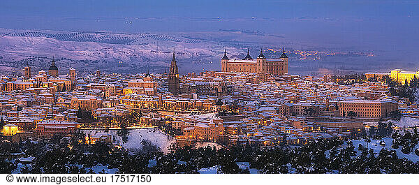 Old town with castle on a snowy hill at sunset and illuminated streets