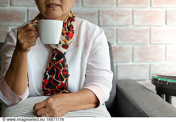 Old woman hold a cup of hot coffee drink at home