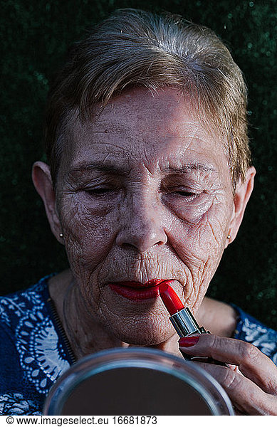 Old woman painting her lips in red looking at herself in the mirror