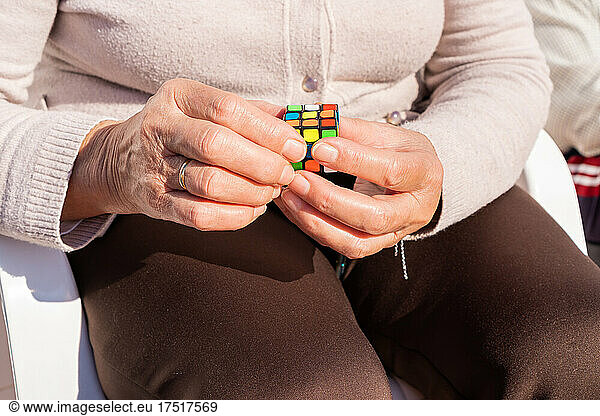 Old woman solving a rubik's cube to improve memory on sunny day