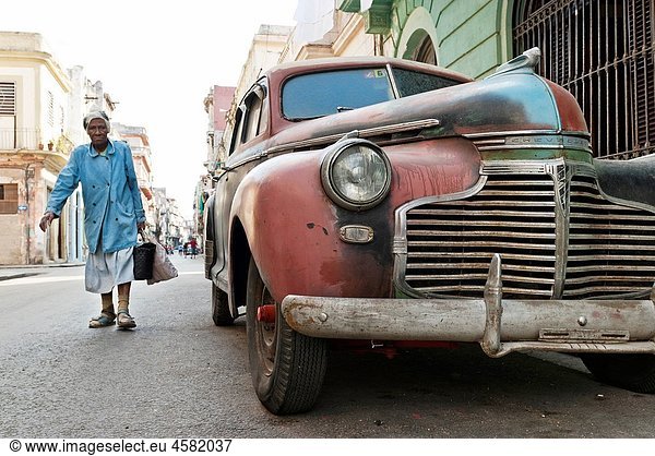 Old woman walking by a vintage car Ciudad de La Habana  Cuba  Caribbean
