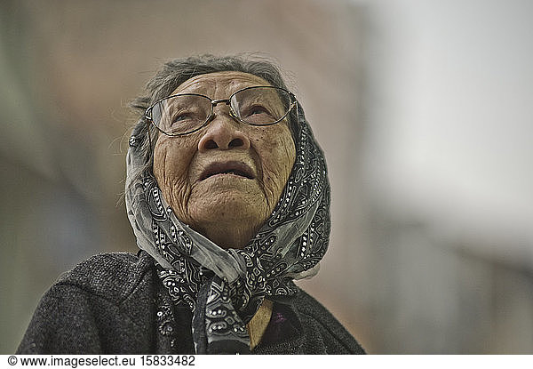 Old woman wears a headscarf and looks up