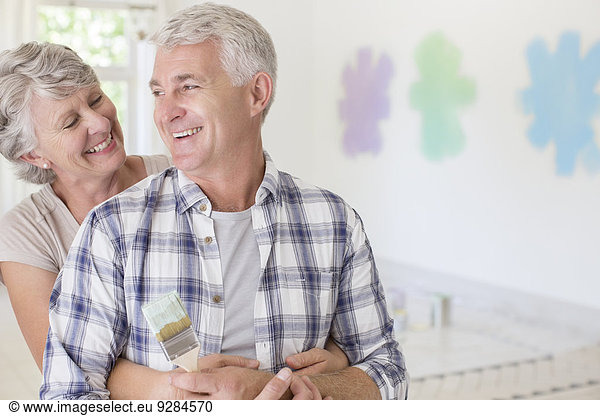 Older couple hugging with paintbrush in living space
