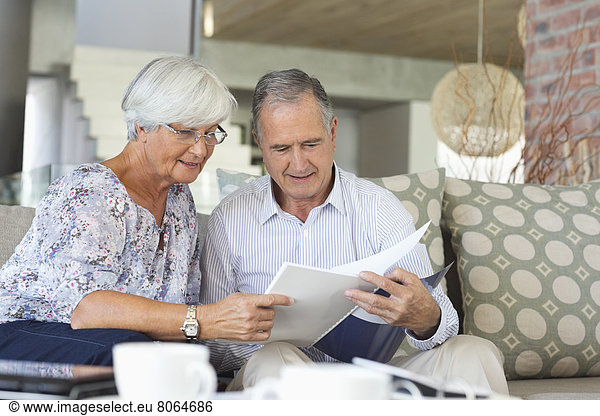 Older couple reading papers together on sofa