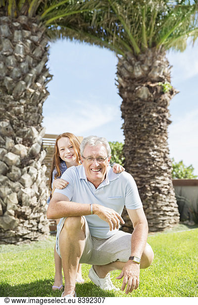Older man and granddaughter smiling in backyard