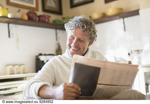Older man reading news paper in kitchen