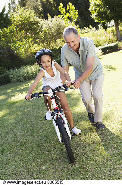 Older man teaching granddaughter to ride bicycle