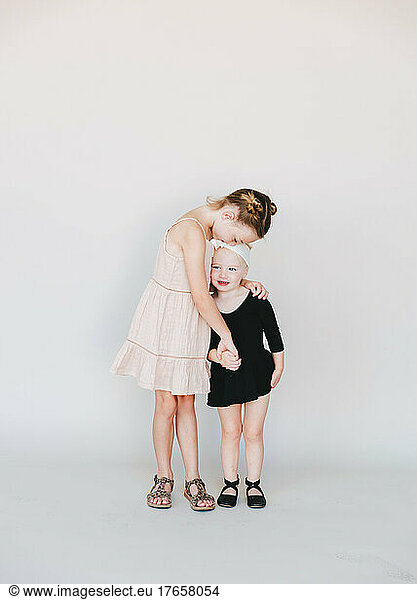 older sister kissing her younger sister in front of a white wall