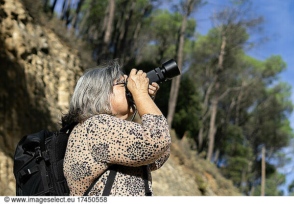 older white-haired woman taking pictures in a forest